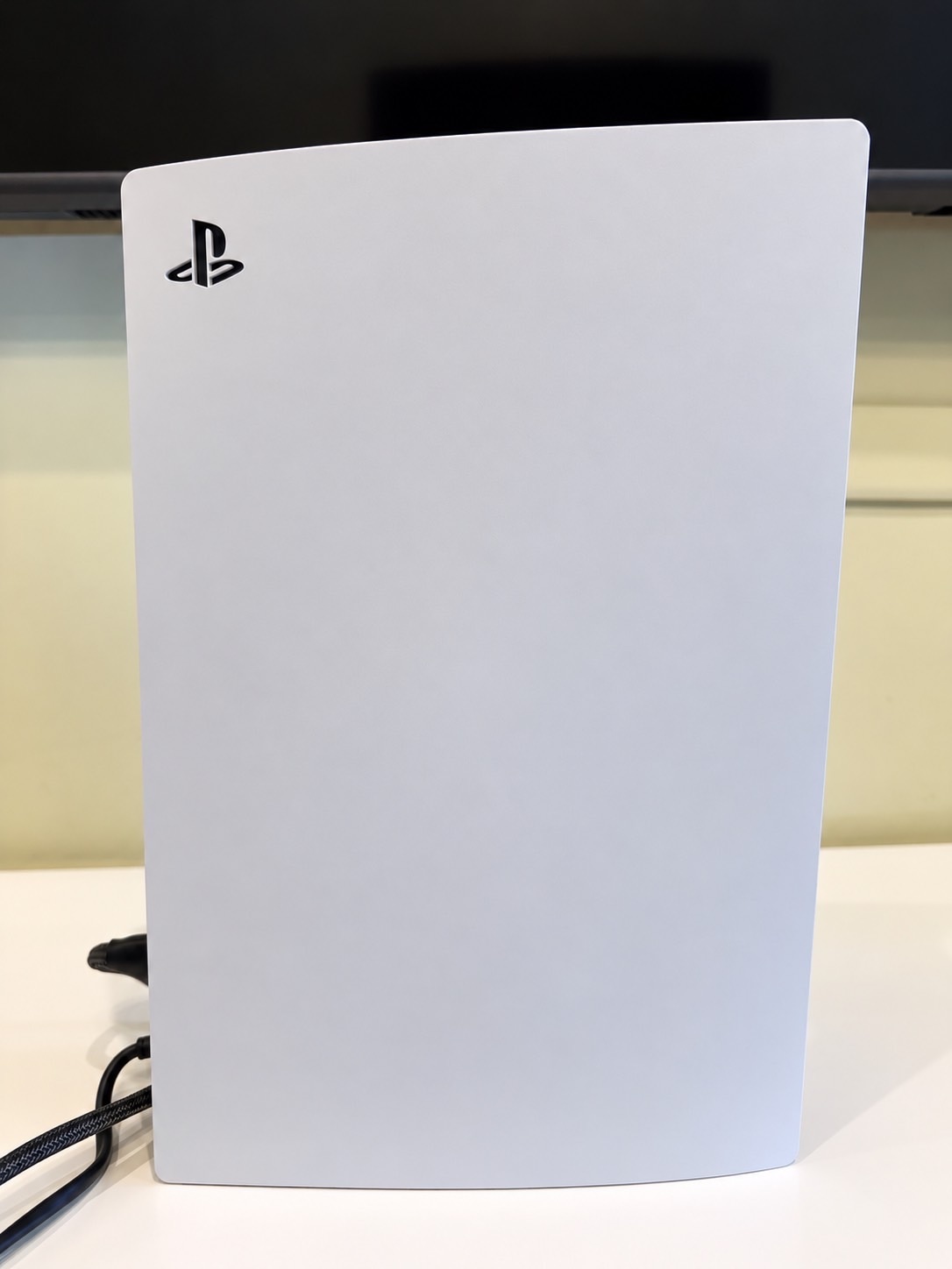 白色 PS5 主機直立擺放在桌上，背後是電視邊框
