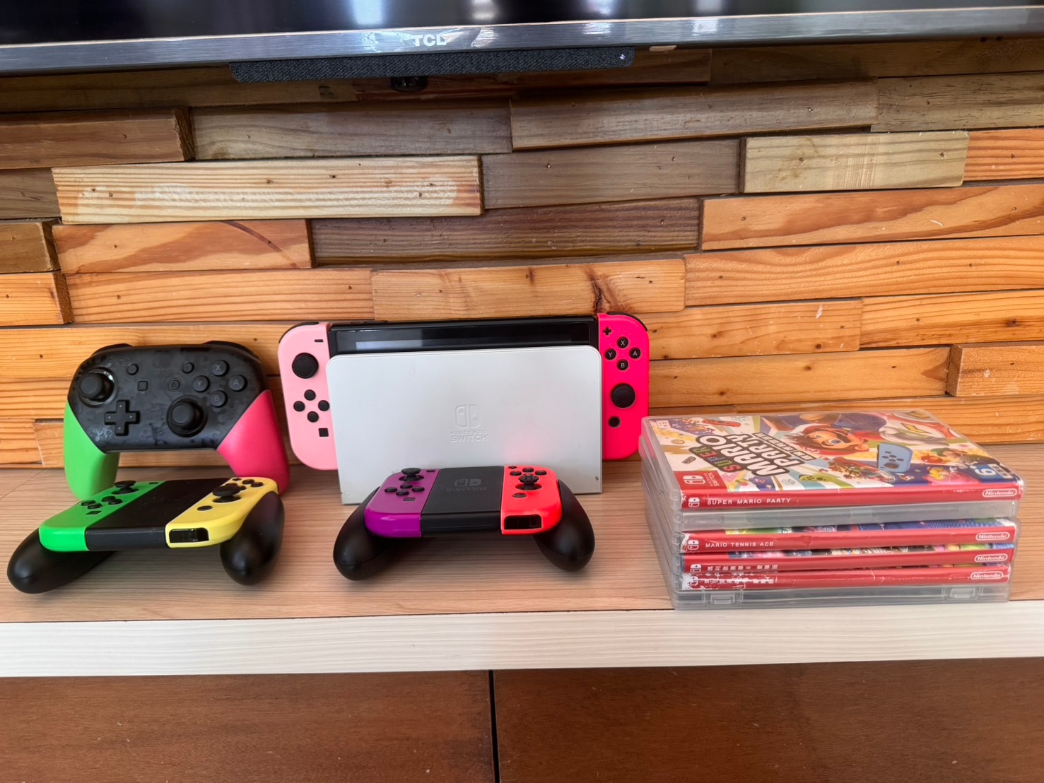 客廳電視下方的 Switch 主機與兩組手把，旁邊疊放瑪利歐系列遊戲片